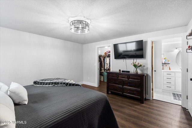 bedroom with a walk in closet, ensuite bathroom, a textured ceiling, dark wood finished floors, and a closet