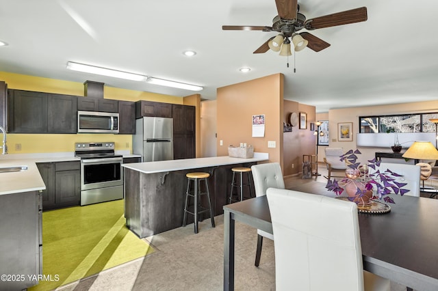 kitchen with a breakfast bar, stainless steel appliances, light countertops, a sink, and dark brown cabinets