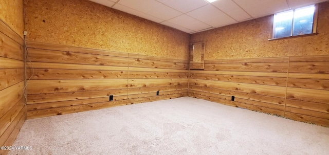 carpeted empty room with a drop ceiling and wooden walls