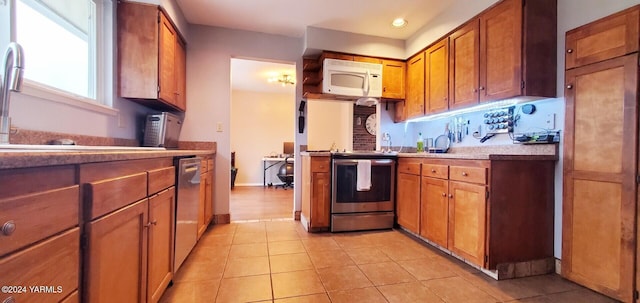 kitchen with light tile patterned floors, stainless steel appliances, light countertops, brown cabinetry, and a sink