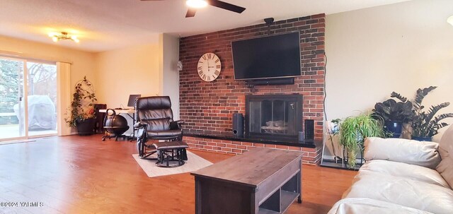 living room with a brick fireplace, a ceiling fan, and wood finished floors