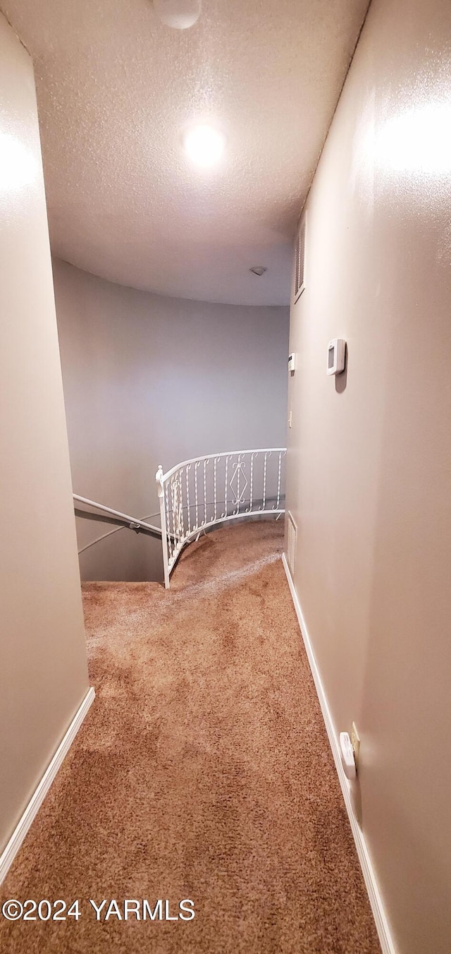 hall featuring a textured ceiling, carpet floors, and baseboards