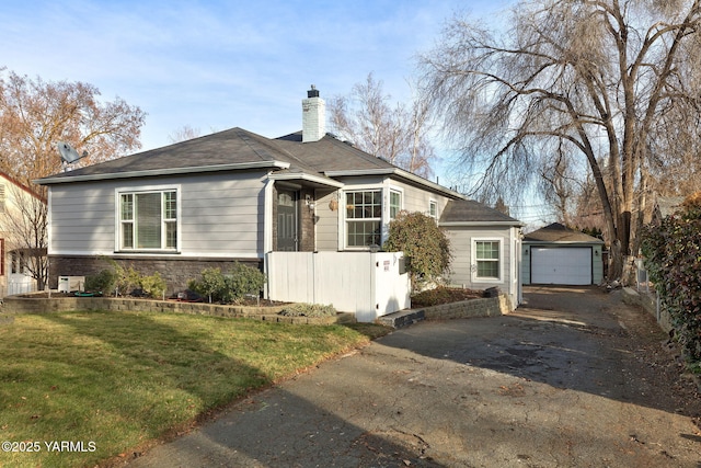 view of front of house featuring driveway, stone siding, a chimney, an outdoor structure, and a front lawn