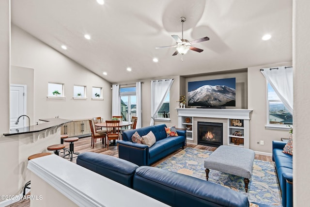 living area with recessed lighting, a glass covered fireplace, light wood-style flooring, and lofted ceiling