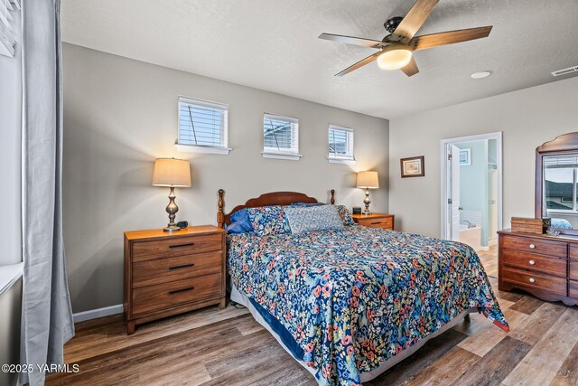 bedroom with visible vents, connected bathroom, baseboards, wood finished floors, and a textured ceiling