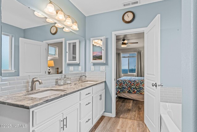 ensuite bathroom with tasteful backsplash, wood finished floors, visible vents, and a sink