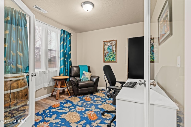 office with visible vents, baseboards, light wood-style floors, and a textured ceiling