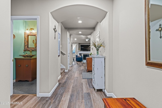 corridor featuring stairway, arched walkways, baseboards, and wood finished floors