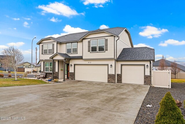 view of front facade with fence, roof with shingles, an attached garage, concrete driveway, and stone siding