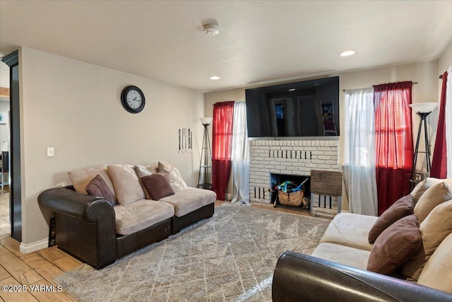 living room featuring light wood-type flooring, a brick fireplace, baseboards, and recessed lighting