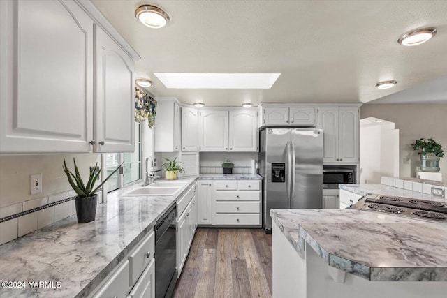 kitchen with a skylight, dark wood finished floors, appliances with stainless steel finishes, white cabinetry, and a sink