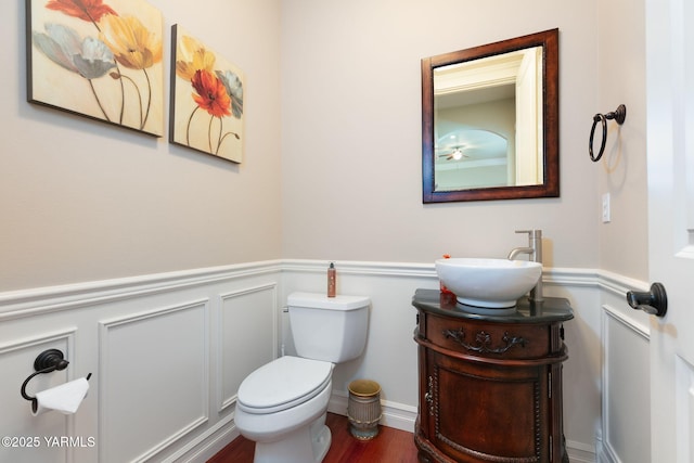 bathroom with vanity, toilet, a wainscoted wall, a decorative wall, and wood finished floors