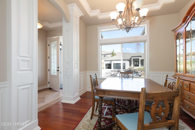 dining room with a decorative wall, dark wood finished floors, arched walkways, a chandelier, and wainscoting