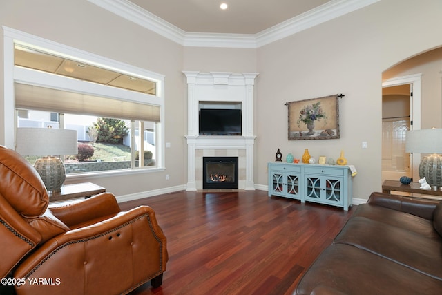 living room with baseboards, ornamental molding, a tiled fireplace, arched walkways, and wood finished floors