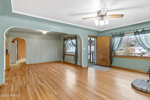 unfurnished room featuring light wood-style floors, ceiling fan, arched walkways, and baseboards