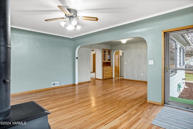 unfurnished living room featuring baseboards, visible vents, arched walkways, ceiling fan, and wood finished floors