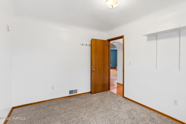 unfurnished room with arched walkways, light carpet, visible vents, and baseboards