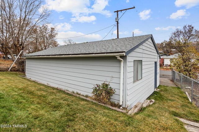 view of property exterior featuring fence, an outdoor structure, a lawn, and roof with shingles