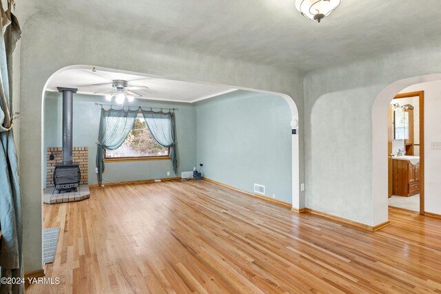 unfurnished living room with a wood stove, visible vents, arched walkways, and wood finished floors