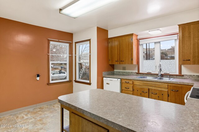 kitchen with brown cabinetry, white appliances, a sink, and baseboards