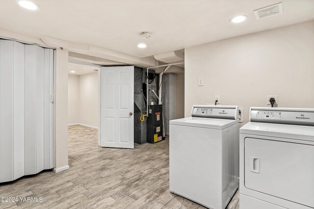 clothes washing area with laundry area, visible vents, washer and dryer, light wood-type flooring, and heating unit