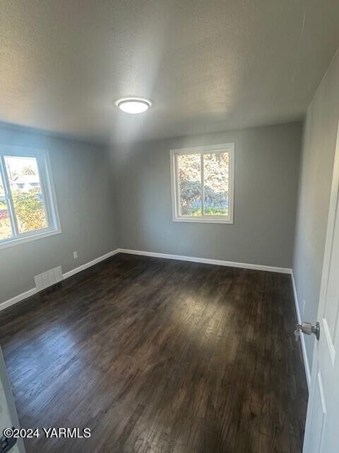 empty room featuring dark wood-style flooring, visible vents, and a healthy amount of sunlight