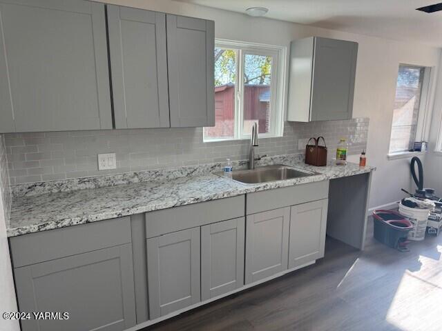 kitchen featuring light stone counters, dark wood-style flooring, backsplash, gray cabinetry, and a sink