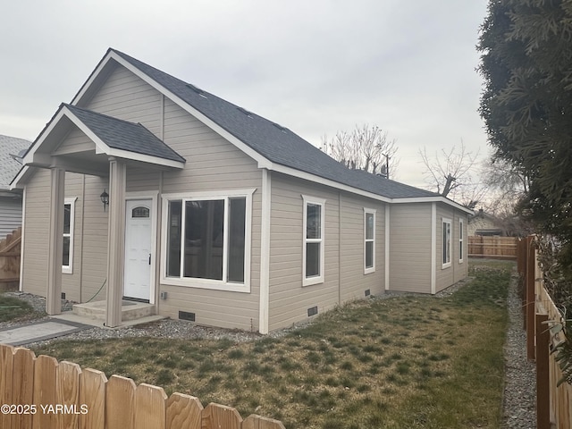 view of front of property featuring entry steps, a shingled roof, a fenced backyard, crawl space, and a front lawn