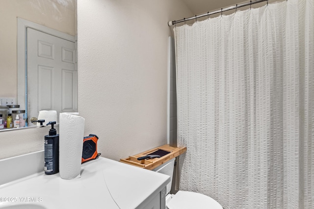 full bath with toilet, vanity, a shower with curtain, and a textured wall