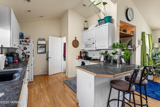 kitchen featuring white appliances, vaulted ceiling, white cabinetry, a kitchen breakfast bar, and light wood-type flooring