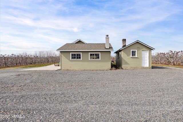 exterior space with an outbuilding, roof with shingles, and a chimney