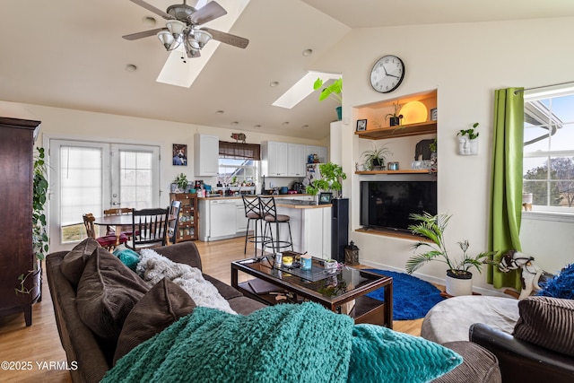 living area with light wood finished floors, vaulted ceiling with skylight, and a ceiling fan