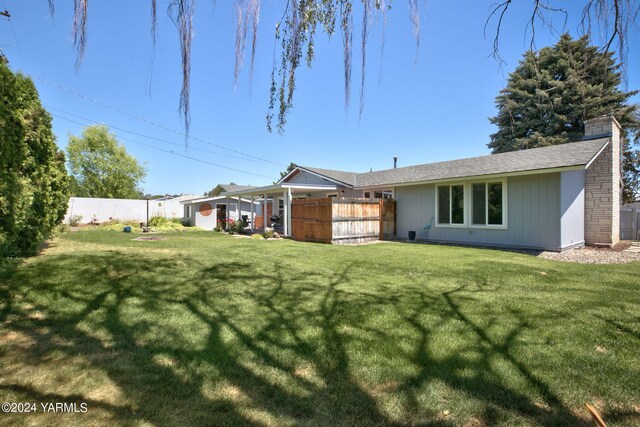 back of property featuring a chimney, fence, and a yard