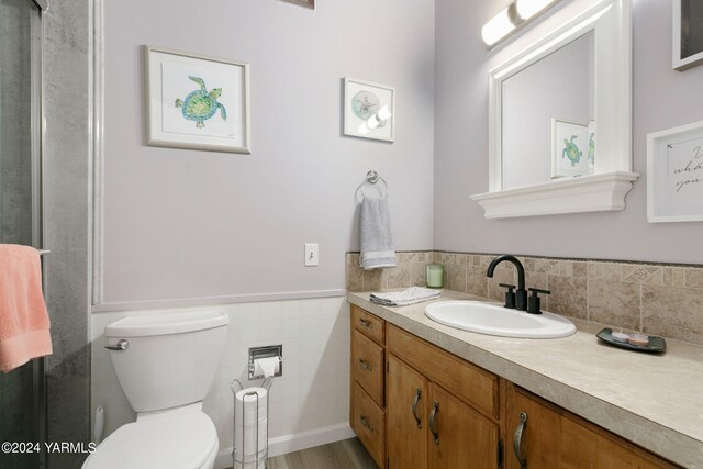 bathroom featuring a wainscoted wall, vanity, toilet, and tile walls