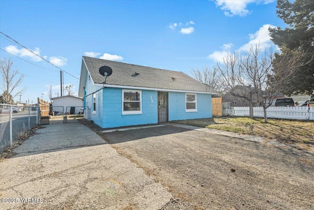 view of front facade featuring driveway, fence, concrete block siding, and roof with shingles