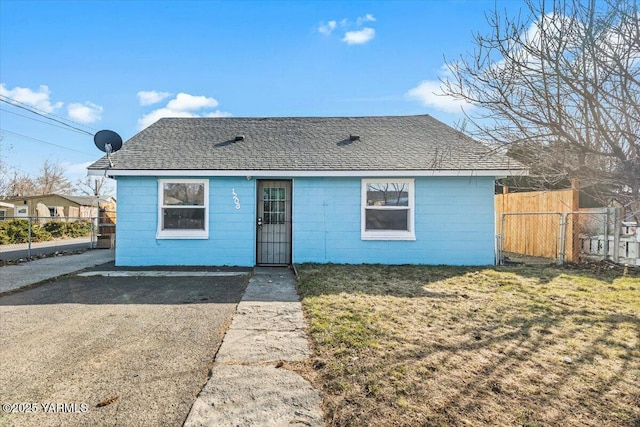 view of front of home with a shingled roof, concrete block siding, fence, and a front lawn