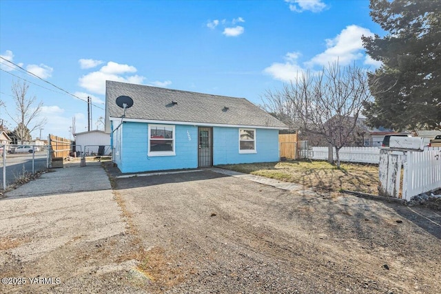 view of front of house featuring driveway, a shingled roof, concrete block siding, and fence