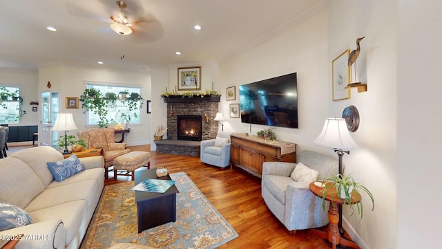 living room with a stone fireplace, recessed lighting, wood finished floors, baseboards, and crown molding