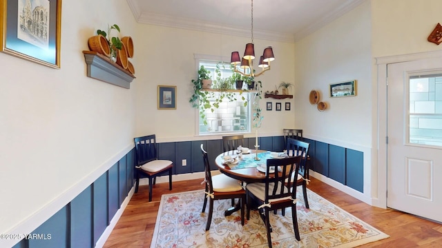 dining area with ornamental molding, wainscoting, wood finished floors, and a notable chandelier