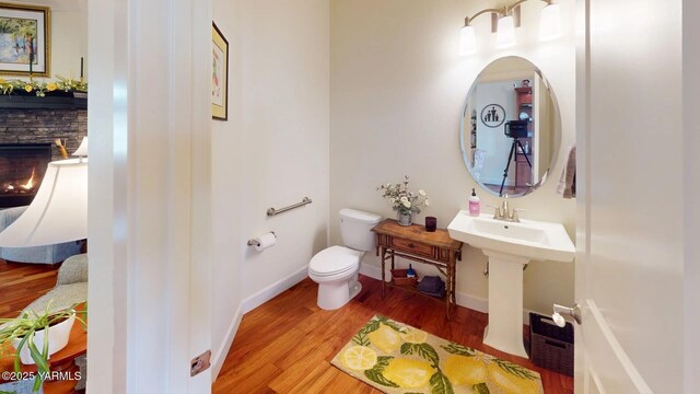 half bath with baseboards, a stone fireplace, toilet, and wood finished floors