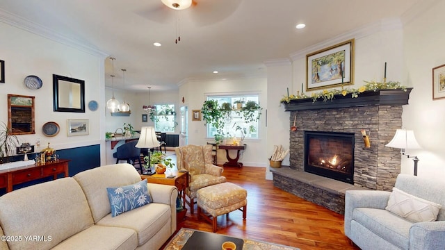 living area with a stone fireplace, recessed lighting, wood finished floors, baseboards, and ornamental molding