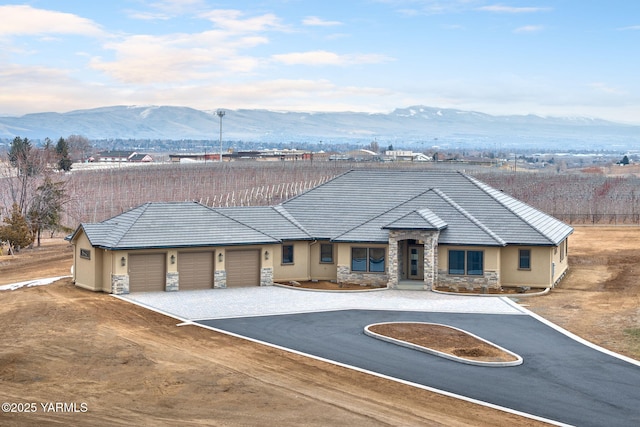 view of front of home with an attached garage, a mountain view, stone siding, driveway, and stucco siding