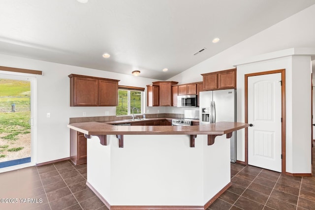 kitchen with stainless steel appliances, a sink, vaulted ceiling, a kitchen breakfast bar, and brown cabinets