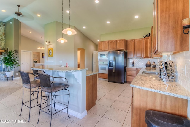 kitchen with arched walkways, hanging light fixtures, a kitchen island, a sink, and white appliances