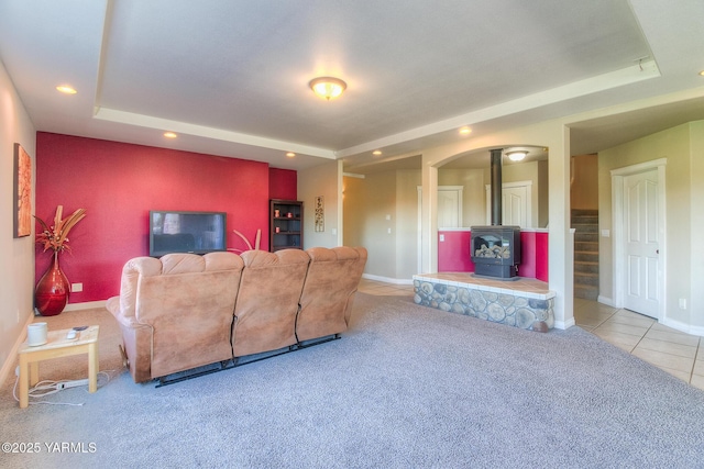 living area with a tray ceiling, a wood stove, light colored carpet, and baseboards