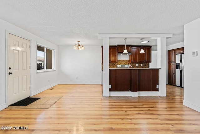 kitchen with stainless steel fridge with ice dispenser, light countertops, light wood-type flooring, decorative backsplash, and an inviting chandelier