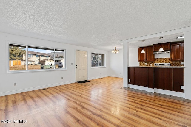 unfurnished living room featuring a textured ceiling, plenty of natural light, light wood-style flooring, and a notable chandelier