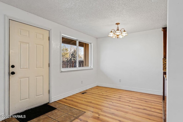 entrance foyer with a notable chandelier, visible vents, light wood-style flooring, a textured ceiling, and baseboards