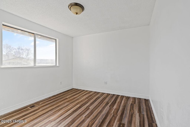 spare room featuring visible vents, a textured ceiling, baseboards, and wood finished floors