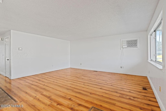 empty room with a wall unit AC, visible vents, a textured ceiling, light wood-type flooring, and baseboards